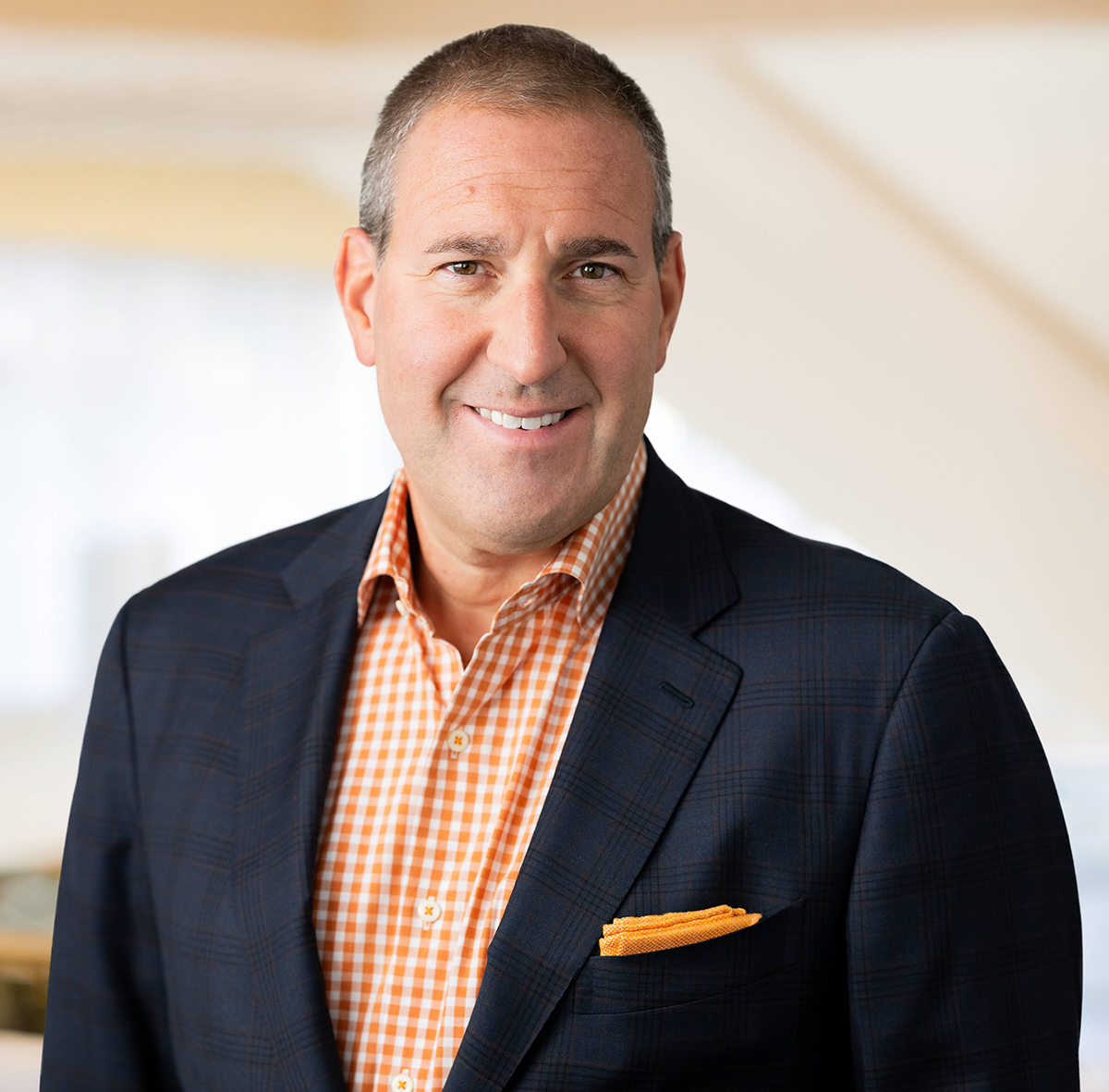 A portrait of a person with short hair, an orange and white collared shirt, and a black suit jacket