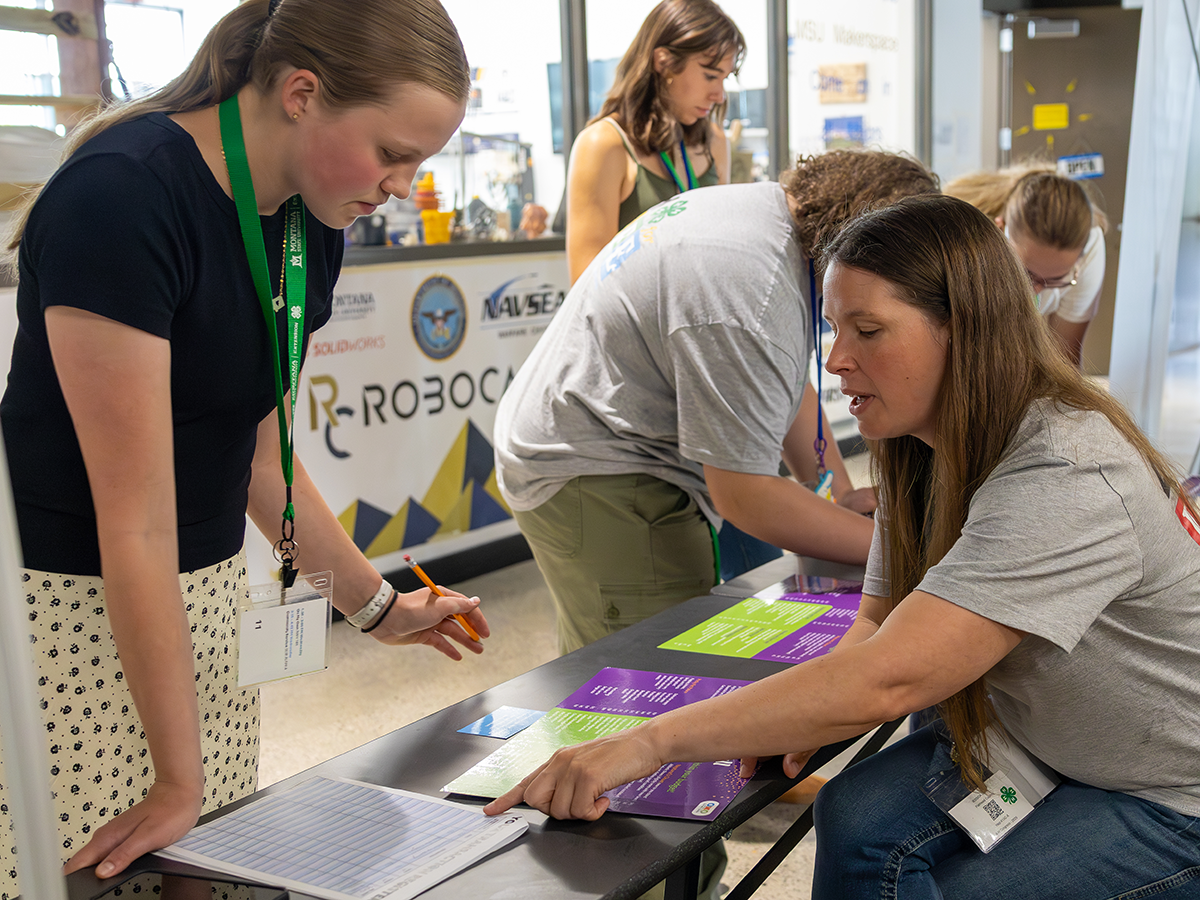 A young girl standing at a table where a young woman is pointing to a paper