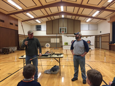 Two 4-H volunteers teaching members how to shoot an arrow