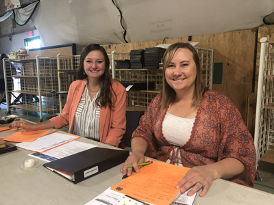 Two 4-H Volunteers smiling and holding documents at a table