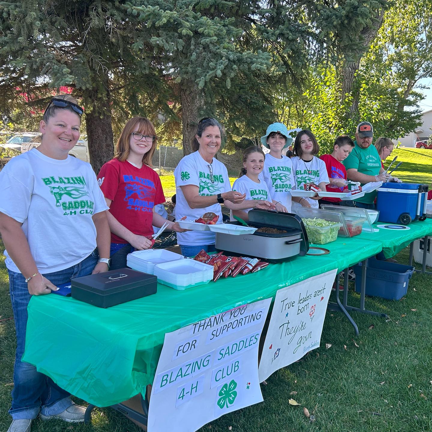 4-H club members and volunteers stand behind a buffet table ready to serve at their fundraiser. (5) Blazing Saddles Club Fundraiser (6) Market Directors Kim and Lorette