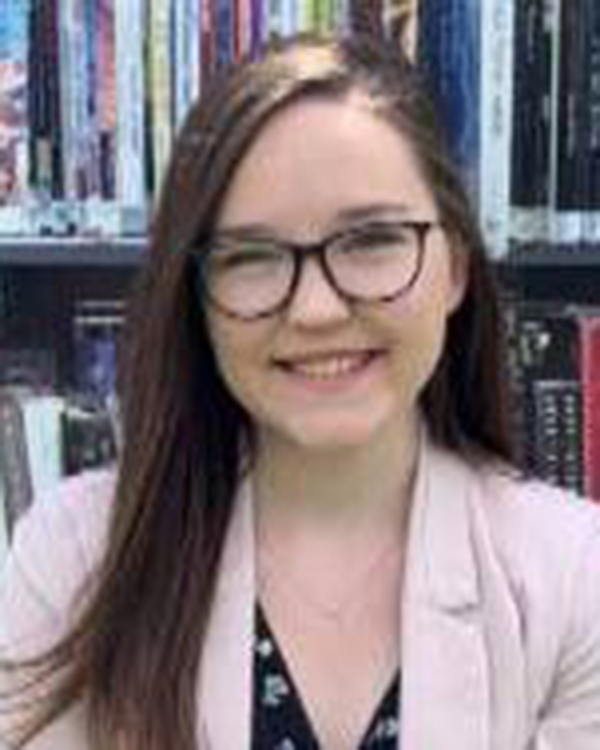 A person with long brown hair wearing a pink blazer and glasses