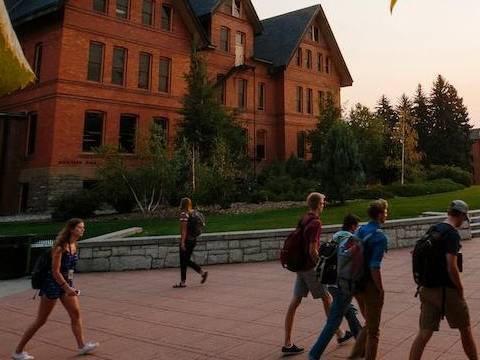 Some students wearing backpacks walking in front of a brick building near sunset