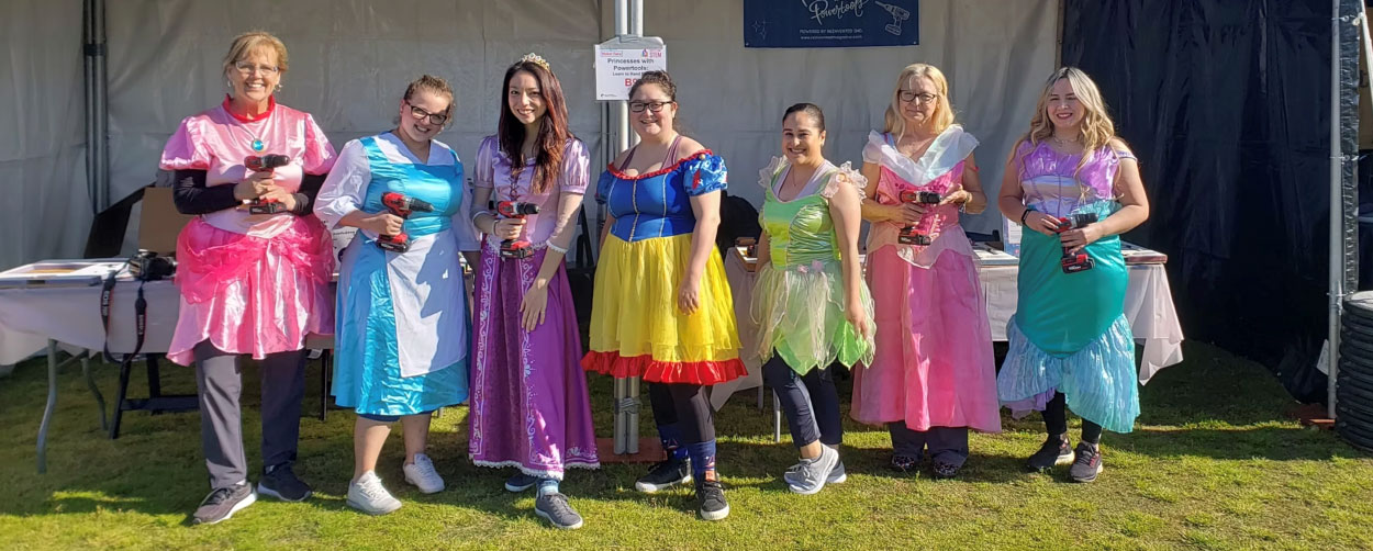 Princesses with Powertools color photo of seven women in various princess costumes; all are holding a power tool